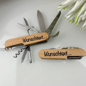 Op de afbeelding: Twee multitools met houten handvatten en diverse roestvrijstalen gereedschappen, waaronder een mes, schaar en kurkentrekker. De tekst "Wunschtext..." staat op het houten handvat. Eén tool is open.