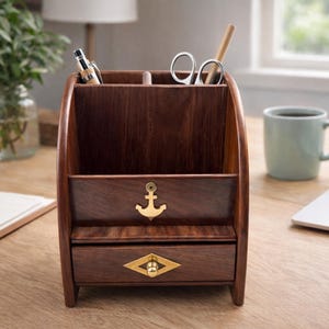 May include: A dark brown wooden desk organizer with multiple compartments for pens, scissors, and other office supplies. It features a drawer with a gold-colored diamond-shaped pull and an anchor emblem. The organizer is on a wooden desk.
