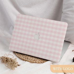 Puede incluir: Un ordenador portátil con una funda de patrón de cuadros rosa y blanco. La funda tiene un recorte para el logotipo de Apple. El portátil está sobre una estera tejida y tela blanca. Las palabras "WITH LOGO" están en un rectángulo naranja claro.
