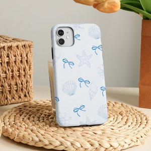 May include: A white phone case featuring a blue and white seashell and starfish pattern. The case has a camera cutout and a blue bow design.