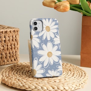 May include: A blue phone case with a white daisy pattern. The case is made of a hard plastic material and has a camera cutout on the back.