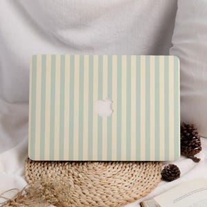 Może przedstawiać: Laptop z jasnym zielono-kremowym wzorem w pionowe paski. Logo Apple jest widoczne z tyłu. Laptop spoczywa na plecionej macie.