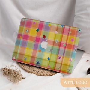 May include: A laptop case with a colorful plaid pattern in shades of pink, yellow, green, and orange. The case is decorated with various star-shaped stickers. The Apple logo is visible on the laptop.