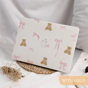 May include: A white laptop case featuring a pink and brown teddy bear design. The case has a pink bow pattern and white polka dots. The case has the text "WITH LOGO" on the bottom right corner.
