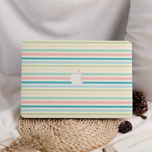Puede incluir: Una funda para portátil con un diseño de rayas pastel en tonos rosa, azul, verde y crema. El logotipo de Apple es visible en el centro. La funda está sobre una esterilla tejida.