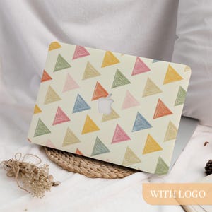 Puede incluir: Una funda para portátil con fondo crema y un patrón de triángulos coloridos dibujados a mano en tonos rosa, naranja, amarillo, verde y azul. El logotipo de Apple es visible. La funda está sobre una esterilla tejida.