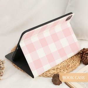 Pu&ograve; includere: Una custodia nera per tablet con un motivo a quadretti rosa e bianco. La custodia &egrave; aperta, rivelando lo schermo del tablet. Le parole "BOOK CASE" sono stampate in basso a destra nell'immagine.