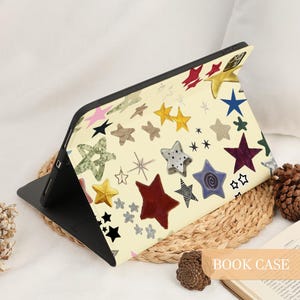 May include: A book case with a cream-colored background and a pattern of colorful stars. The stars are in various colors and designs, including gold, red, blue, and silver. The text "BOOK CASE" is visible in the bottom right corner.