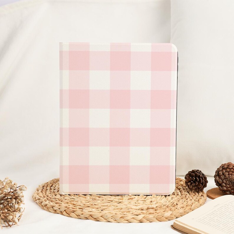 Pu&ograve; includere: Un quaderno con motivo a quadri rosa e bianco. Il quaderno &egrave; rettangolare e ha una copertina rigida. &Egrave; appoggiato su un sottobicchiere intrecciato. Lo sfondo &egrave; un morbido tessuto bianco.