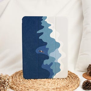 Puede incluir: Funda para tableta con un diseño abstracto de océano. La funda representa un barco en el agua, con tonos azules y blancos. La funda está sobre una estera tejida.