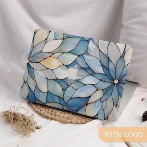 May include: A laptop with a floral design case. The case has a blue and white stained glass-style pattern with a central flower motif. The Apple logo is visible. The laptop is on a woven mat.