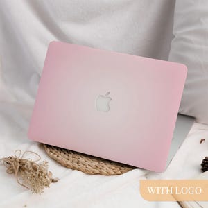 Könnte beinhalten: Ein rosa Laptop mit dem Apple-Logo auf dem Deckel, auf einer gewebten Matte und weißem Stoff. Die Worte "WITH LOGO" befinden sich in einem hellorangen Rechteck unten rechts.