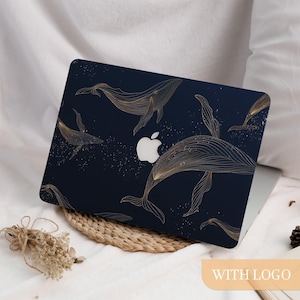 Op de afbeelding: Een marineblauwe laptophoes met een gouden lijntekening van walvissen die in een sterrenzee zwemmen. De hoes heeft een wit Apple-logo. De laptop staat op een witte ondergrond.