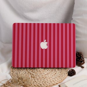 May include: A laptop case featuring a pattern of red and pink vertical stripes, with the Apple logo centrally placed. The case is rectangular and rests on a woven mat. The case is designed to fit a laptop.