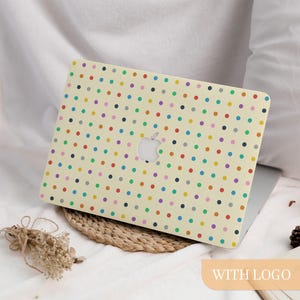 May include: A laptop with a cream-colored cover featuring a pattern of colorful polka dots. The cover has a cutout for the Apple logo. The laptop is resting on a woven mat and white fabric. The words "WITH LOGO" are in a light orange rectangle.