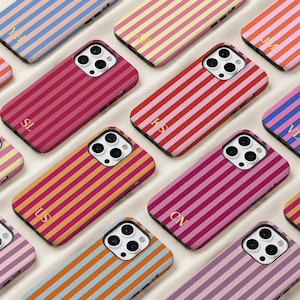 May include: A collection of smartphone cases featuring vertical stripes in various colour combinations, including pink, red, orange, yellow, and blue. Each case has a camera cutout and gold-coloured initials printed on the lower section.