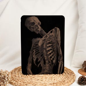 May include: A black tablet case featuring a detailed pencil drawing of a human skeleton. The skeleton is depicted in a three-quarter view, with the skull and rib cage prominently displayed against a dark background. The artwork has a realistic, anatomical style.