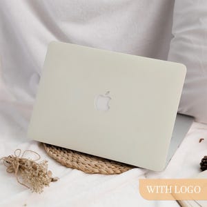 May include: A light beige laptop with the Apple logo on the lid. The laptop is resting on a woven mat and white fabric. The words "WITH LOGO" are in a light orange rectangle.