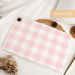Pu&ograve; includere: Custodia per tablet con motivo a quadri rosa e bianchi. La custodia &egrave; aperta, rivelando l'interno. Le parole "BOOK CASE" sono stampate su uno striscione marrone chiaro nell'angolo in alto a destra.