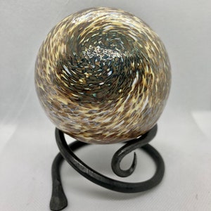 May include: A decorative glass sphere with a swirling pattern of brown, tan, and white. The sphere sits on a black, wrought-iron stand with a curved, spiral design. The overall aesthetic is artistic and decorative.