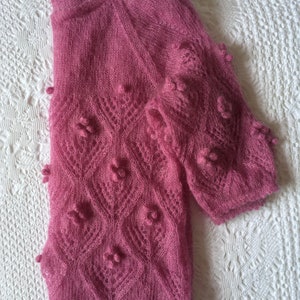 May include: A pink knitted sweater with a delicate lace pattern and small, raised bobbles. The sweater has a slightly loose fit and a round neckline.