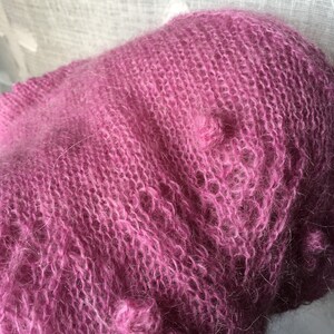 May include: A soft, pink mohair yarn with a fuzzy texture. The yarn is loosely knit and has a delicate, airy feel.