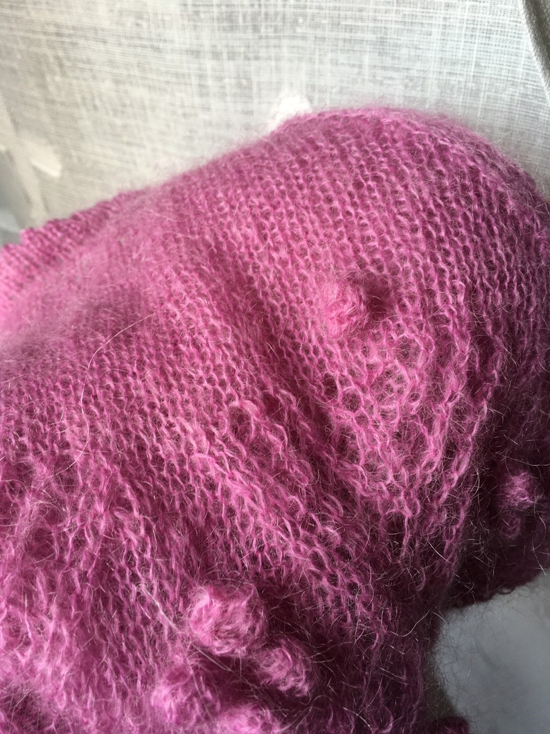 May include: A soft, pink mohair yarn with a fuzzy texture. The yarn is loosely knit and has a delicate, airy feel.