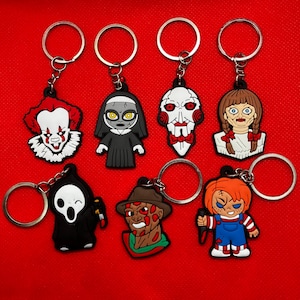 Może przedstawiać: Zestaw 8 breloków z postaciami z filmów grozy. Breloki przedstawiają postacie z popularnych filmów grozy, takich jak Pennywise the clown, Freddy Krueger, Chucky i inne. Breloki są wykonane z czarnej i czerwonej gumy i mają srebrne kółka do kluczy.