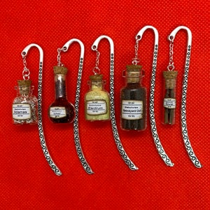 May include: Six silver bookmark charms with glass vials filled with glitter and labeled with names like "Adamas", "Ichor", "Electum", "Graveyard Dirt", and "Rowan".