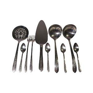May include: A collection of vintage silverware, including serving spoons, forks, and a cake server. The silverware has ornate floral detailing and a shiny, reflective surface. The set is arranged on a white background.
