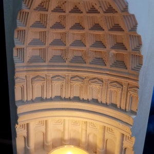 May include: A white plaster candle holder shaped like a dome with a small candle inside. The dome has a detailed design of arches and columns.