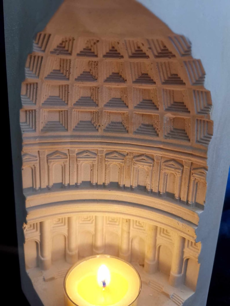 May include: A white plaster candle holder shaped like a dome with a small candle inside. The dome has a detailed design of arches and columns.