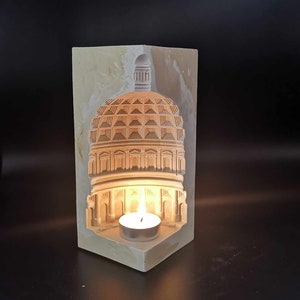 May include: A white plaster candle holder shaped like a dome with a small candle inside. The candle is lit and casting a warm glow.