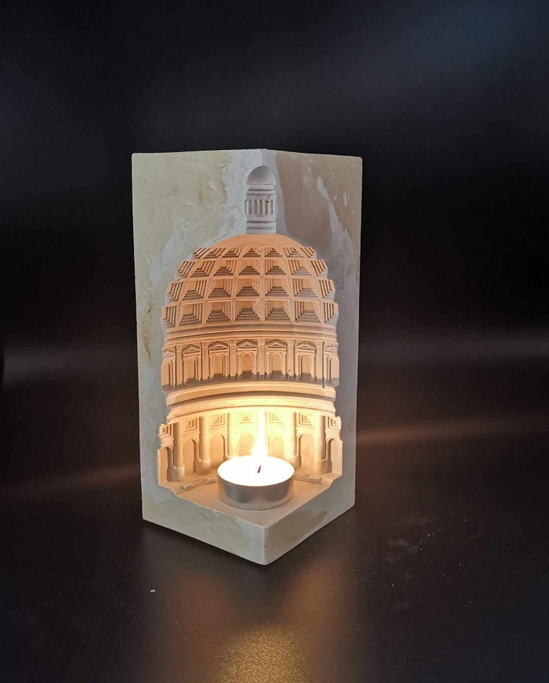 May include: A white plaster candle holder shaped like a dome with a small candle inside. The candle is lit and casting a warm glow.