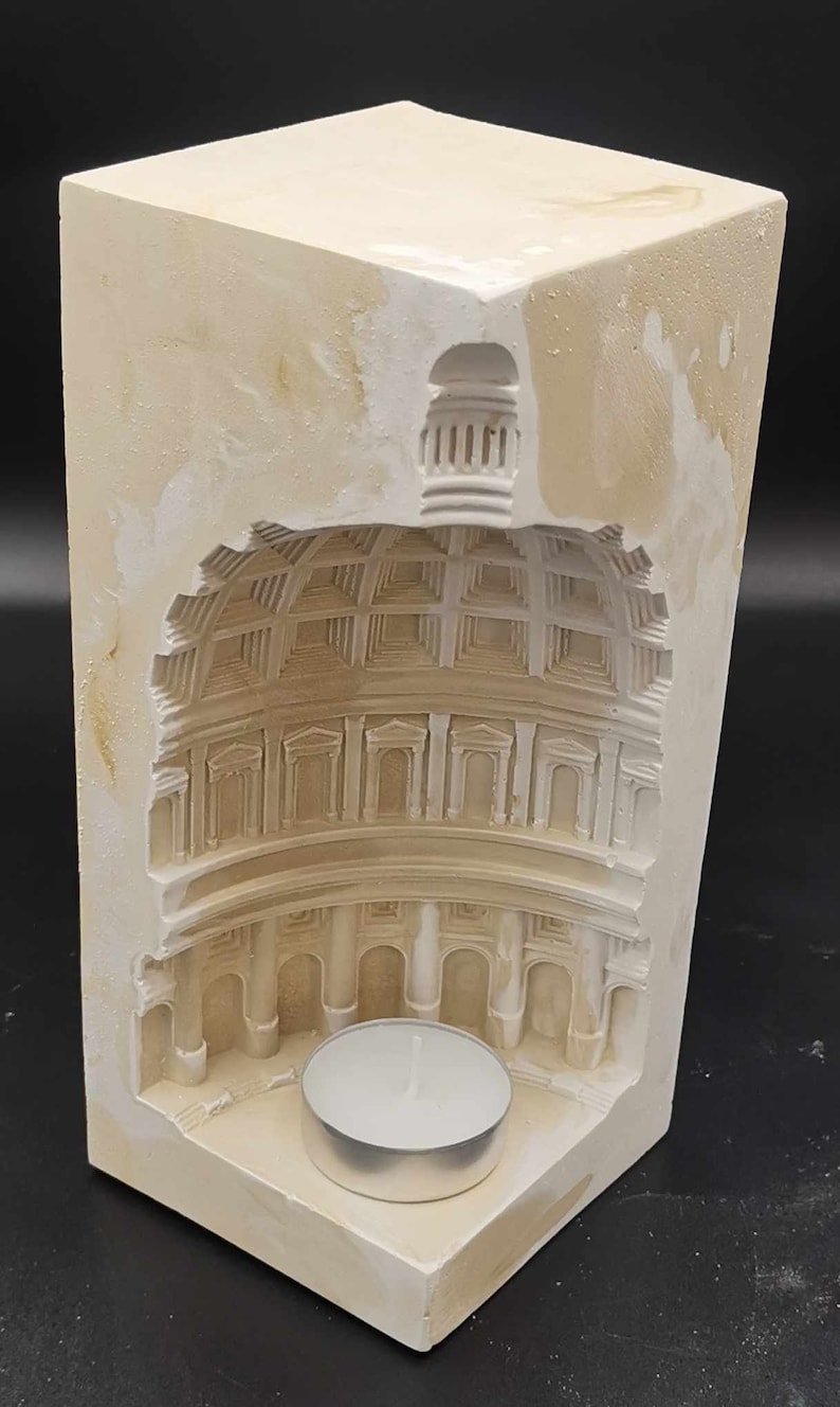 May include: A white plaster candle holder shaped like a building with a dome. The candle holder has a small, round opening for a tea light candle.