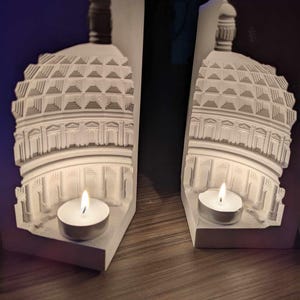 May include: Two white bookends shaped like a dome building with a candle holder in each. The candles are lit and glowing.