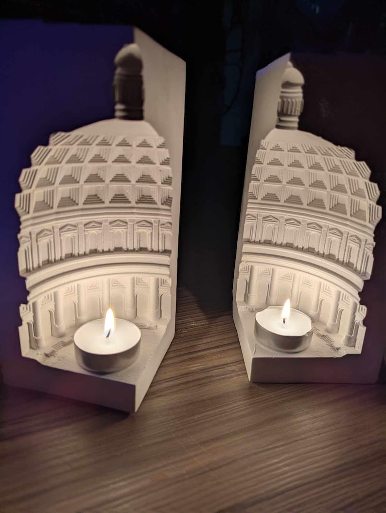 May include: Two white bookends shaped like a dome building with a candle holder in each. The candles are lit and glowing.