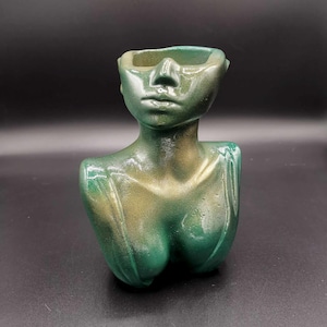 May include: A green and gold bust sculpture of a person wearing sunglasses. The sculpture has a hollow top that can be used as a planter.