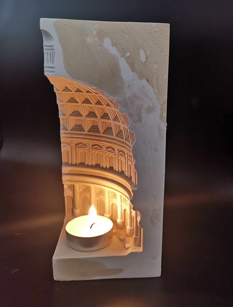 May include: A white plaster candle holder shaped like a Roman building with a lit tea light candle inside.