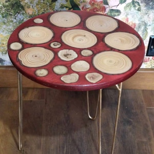 May include: A round wooden table with a red top and gold metal legs. The top is decorated with a mosaic of wood slices, each with a unique grain pattern.