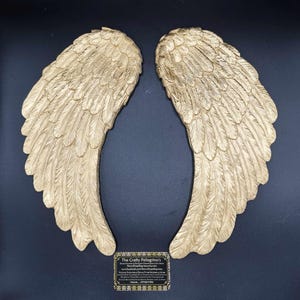 May include: A pair of large, gold-painted angel wings with detailed feather designs. The wings are made of a lightweight material and are perfect for adding a touch of whimsy to any space.