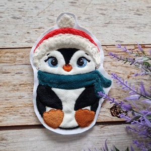 Könnte beinhalten: Ein weißer Filz-Pinguin, der eine rot-weiße Weihnachtsmütze und einen türkisfarbenen Schal trägt. Der Pinguin hat schwarze Augen und einen schwarzen Schnabel.