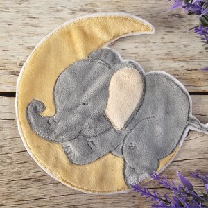Könnte beinhalten: Ein grauer Plüschelefant mit einem gelben Halbmond dahinter. Der Elefant schläft mit geschlossenen Augen und seinem eingerollten Rüssel. Der Mond hat einen weißen Rand.