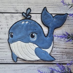 Op de afbeelding: Een blauwe walvis-applique met een witte buik en een zwarte omtrek. De walvis heeft een kleine spuit op de bovenkant van zijn kop en grote, zwarte ogen.