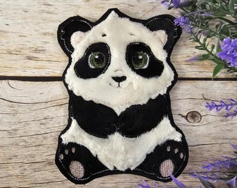 May include: A plush panda bear applique with black and white fur. The panda has a black nose and black eyes with green pupils. The panda is sitting with its paws in front of it.