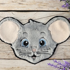 Op de afbeelding: Een grijs vilten muizenhoofd met zwarte geborduurde ogen en een roze neus. De oren zijn van wit vilt.