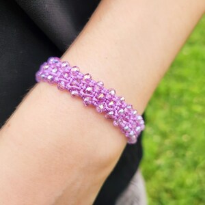 Peut inclure: Un bracelet en perles violettes avec des perles irisées tissées dans le cordon.