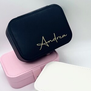 May include: Three jewellery boxes, one black with the name "Andrea" in gold lettering, one pink, and one white.