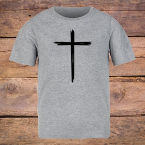 May include: A gray t-shirt with a black cross graphic. The cross is stylized with a brushstroke effect.