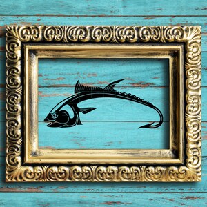 May include: A black silhouette of a fish with a long, thin tail is framed in a gold ornate picture frame. The frame is against a blue wooden background.